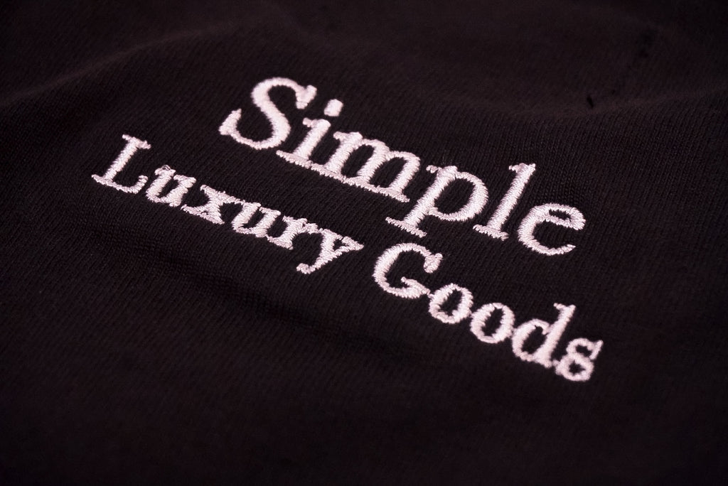 Close-up of a black fabric surface with white embroidered text reading 'Simple Luxury Goods'.