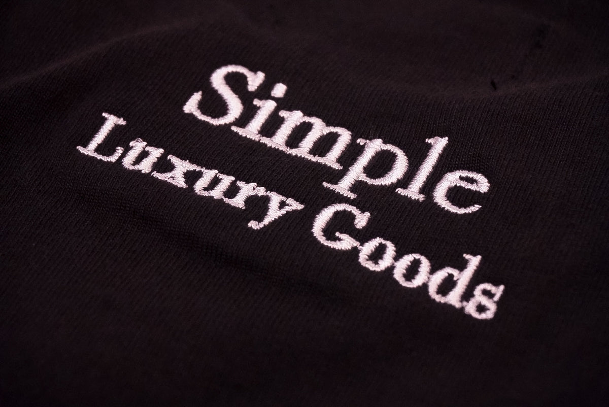 Close-up of a black fabric surface with white embroidered text reading 'Simple Luxury Goods'.