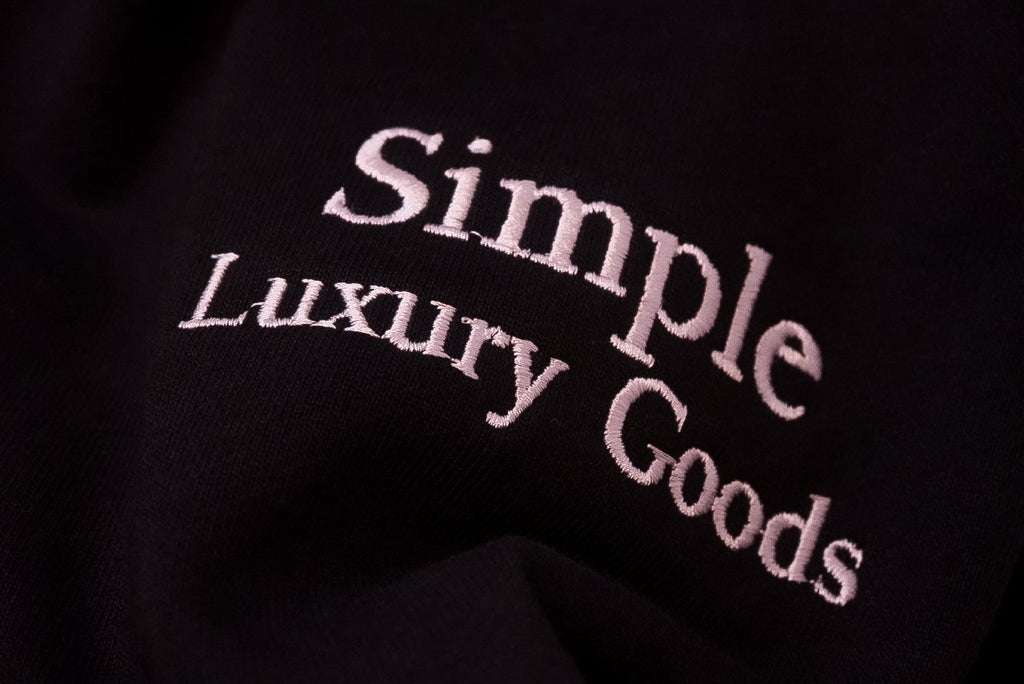 Close-up of a black fabric surface with the words 'Simple Luxury Goods' embroidered in a white script.