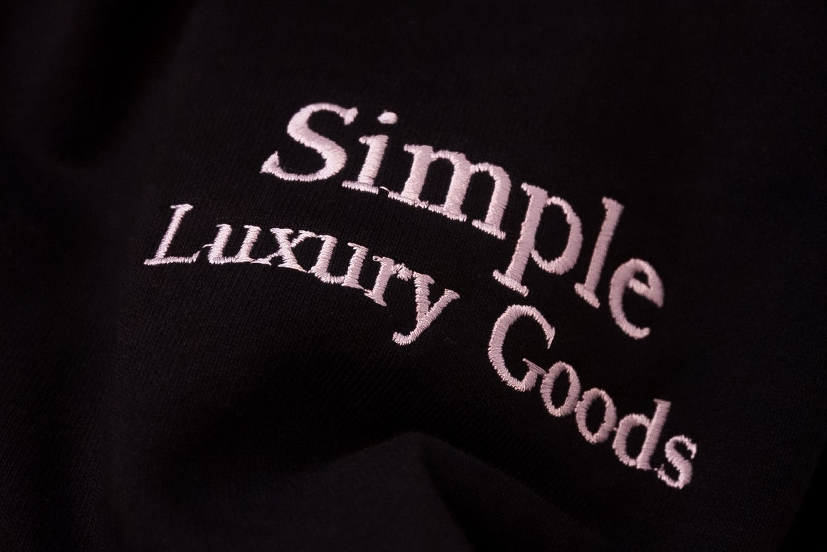 Close-up of a black fabric surface with the words 'Simple Luxury Goods' embroidered in a white script.