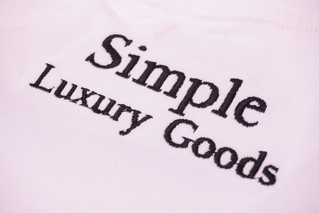Close-up of a white fabric surface with black embroidered text reading 'Simple Luxury Goods'.