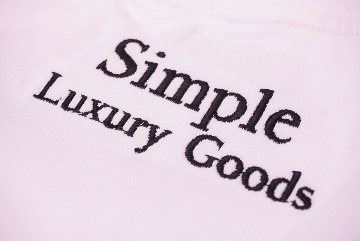 Close-up of a white fabric surface with black embroidered text reading 'Simple Luxury Goods'.