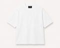 A plain white, slightly oversized, short-sleeve crewneck t-shirt laid flat against a light off-white background. A black woven label is visible inside the collar, reading 'Simple Luxury Goods'