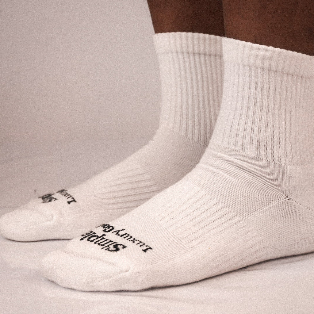 A pair of white ribbed quarter socks worn on feet, with black jacquard knitted branding text visible on the toes.